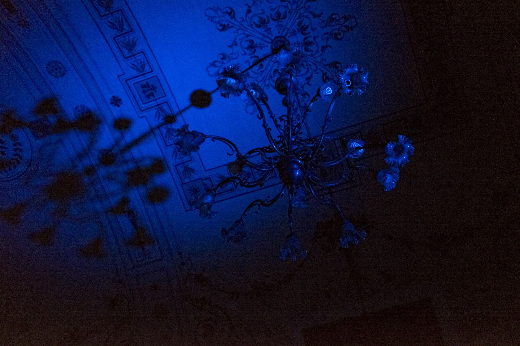 The original dark chandelier and ceiling under intense blue lighting