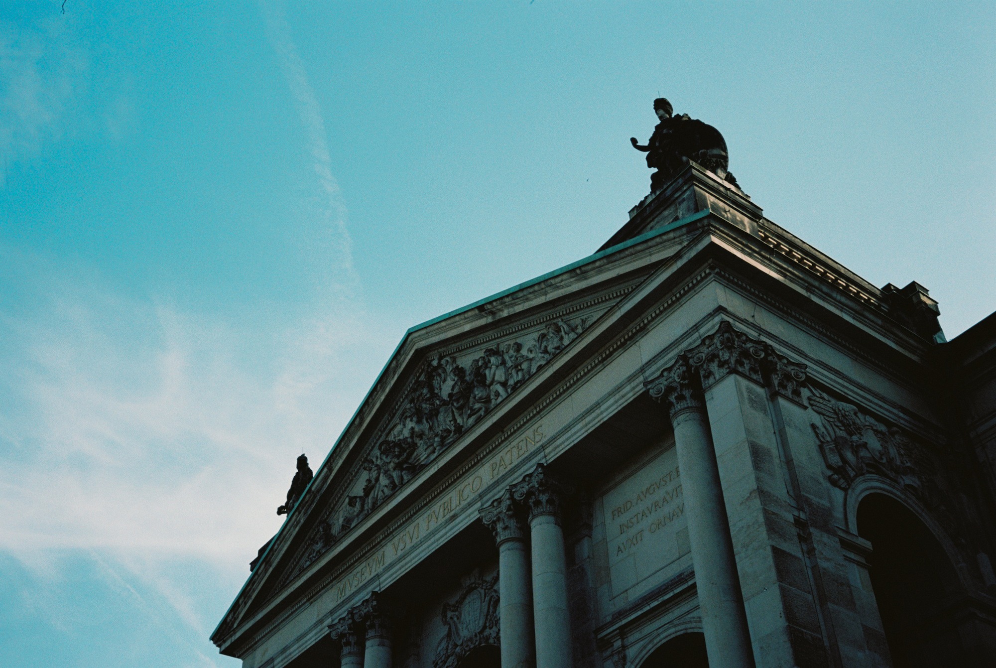 The original film photograph of a building and statue, with a cyan-green cast and small marks.
