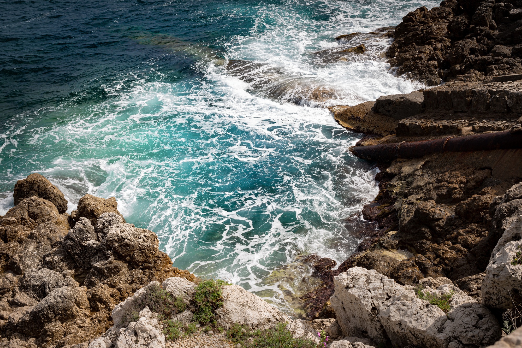 Turquoise waves and white foam swirling between warm limestone rocks.