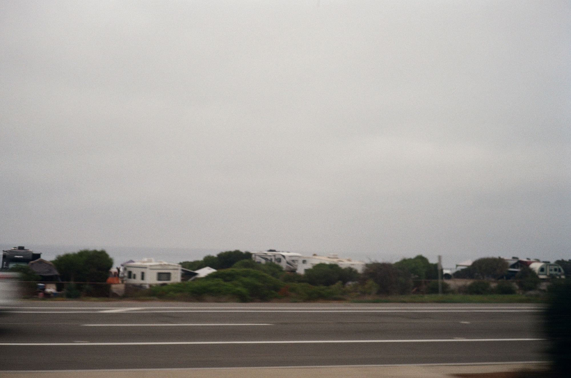 The original color photograph of a road and campers by the coast, with a pale sky and motion blur.