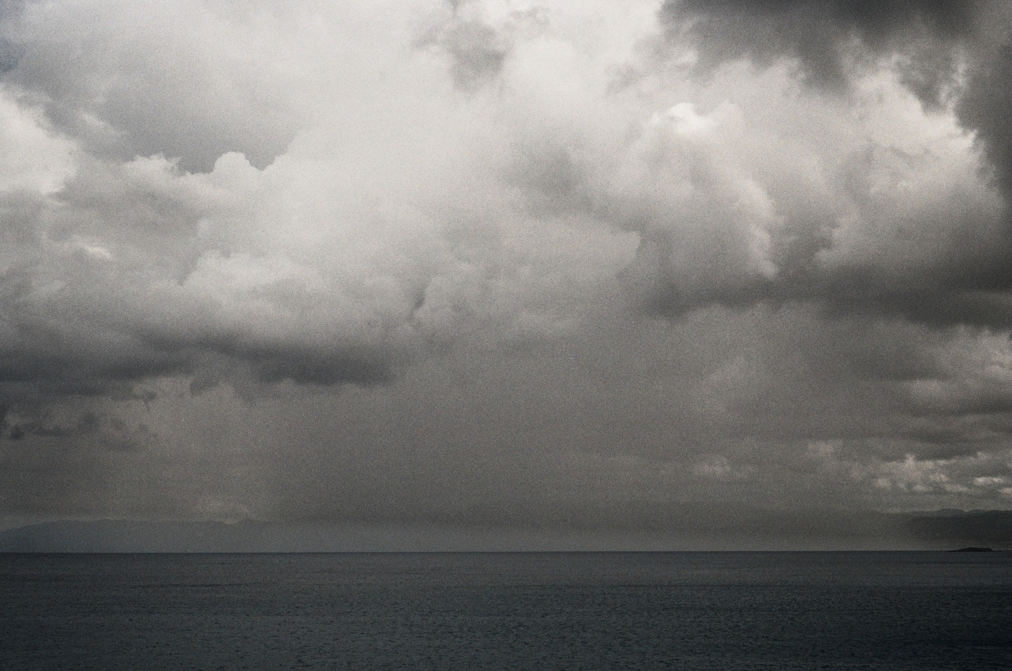 A dark sea beneath heavy, layered clouds, with restrained cool color and visible film texture.