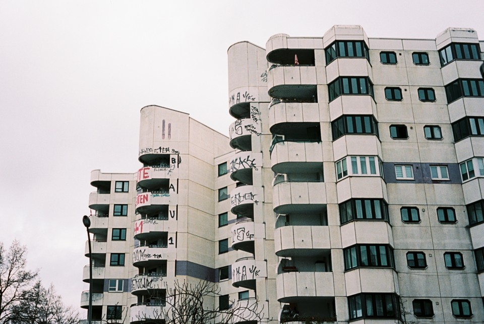 Pale concrete apartment blocks with curved balconies, dark windows and delicate film texture
