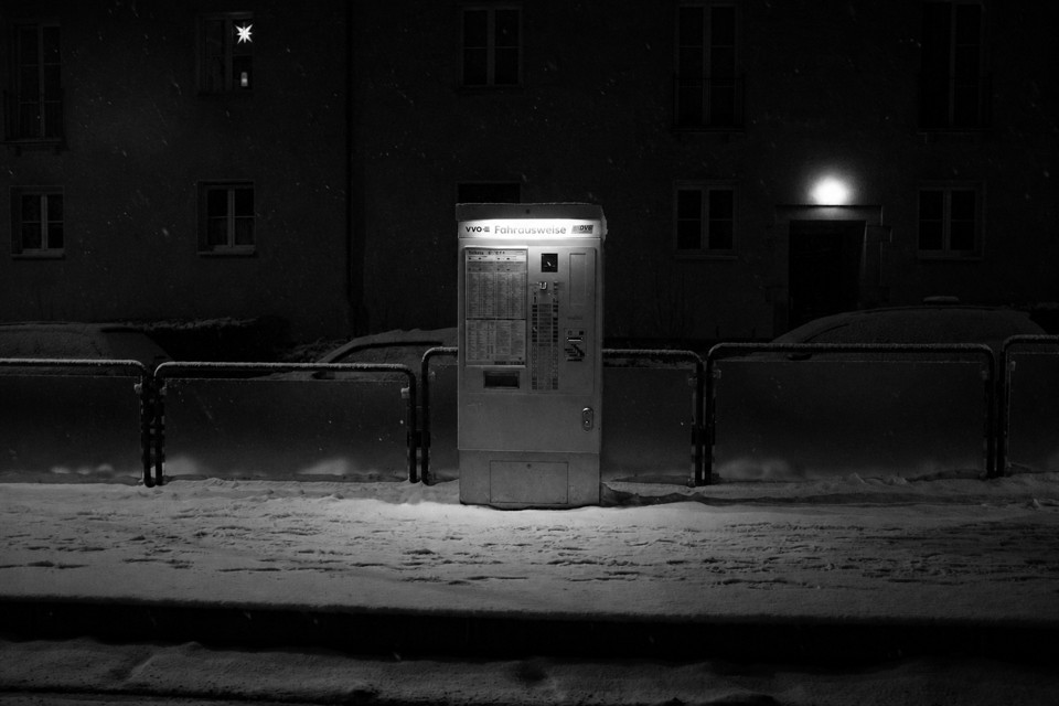 Black-and-white night photograph of an illuminated ticket machine in snow